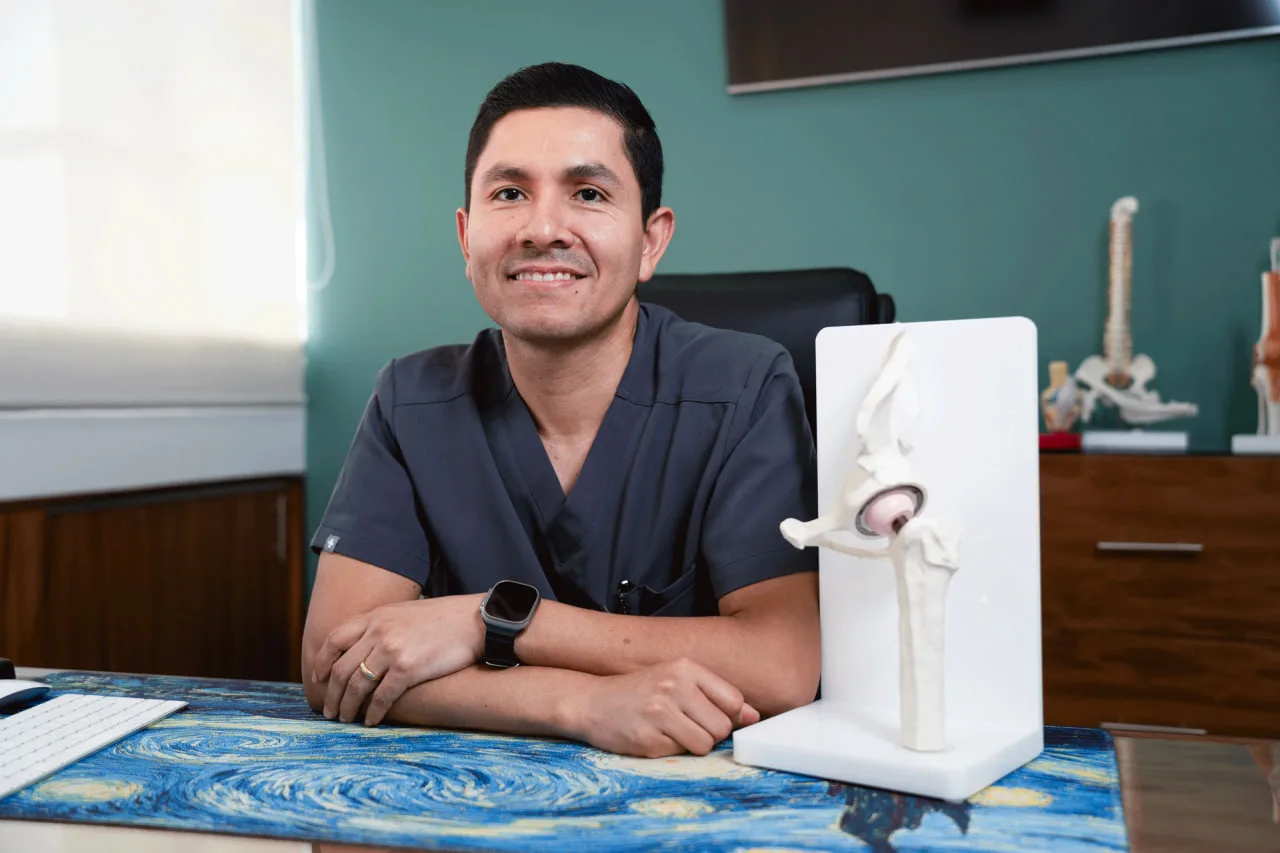 Dr. Galvis smiling in his office next to a hip model